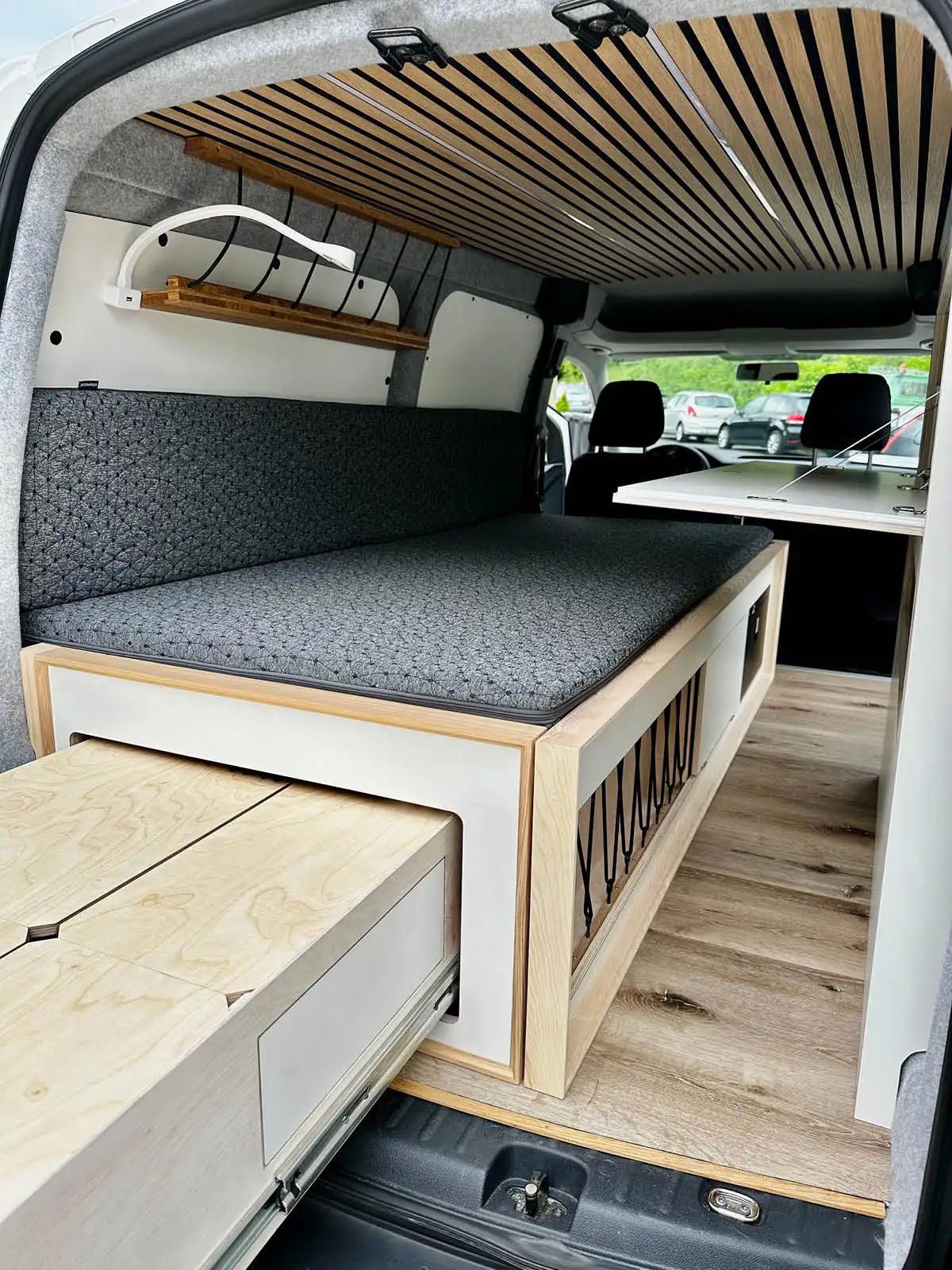 Innenraum des VW Caddy Lina mit Bettmodul, Holzlatten und Stauraum